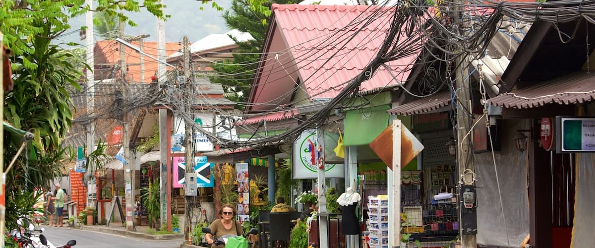 A street with motorcycles parked on the side, a person riding a motorcycle, and various shops with signs.