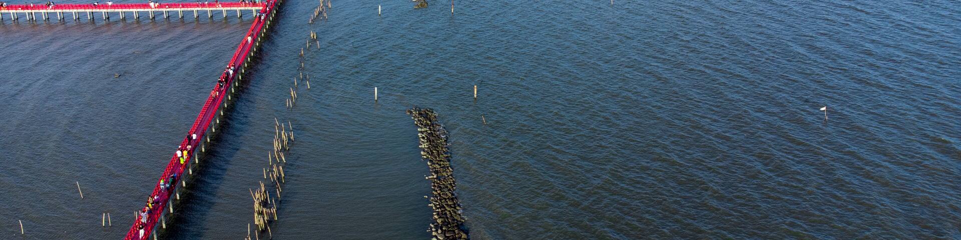 Photo on drone with Beautiful wooden long red bridge at seaside of samut sakhon province,Thailand. Locate on dolphin view point called mutshanu shring.