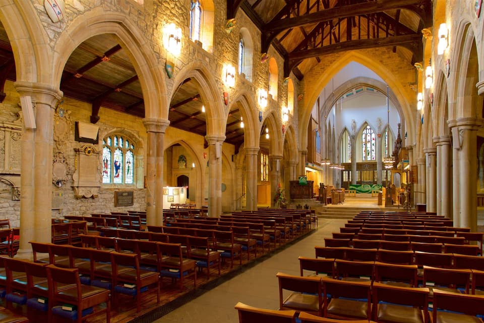 An interior of a church with wooden pews, stone arches, and stained glass windows.