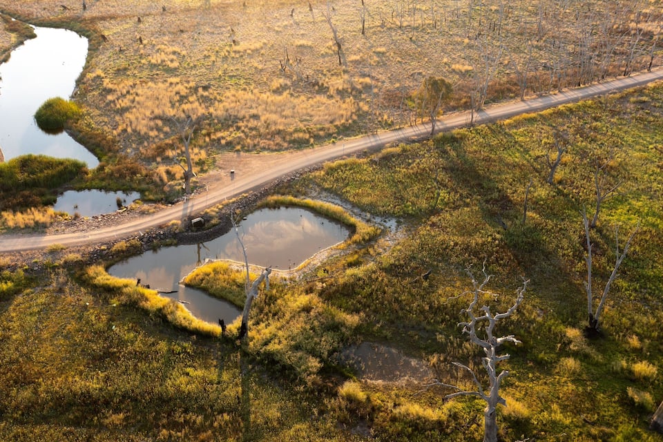 Un camino de tierra serpentea por una zona húmeda con varios estanques pequeños y vegetación escasa.