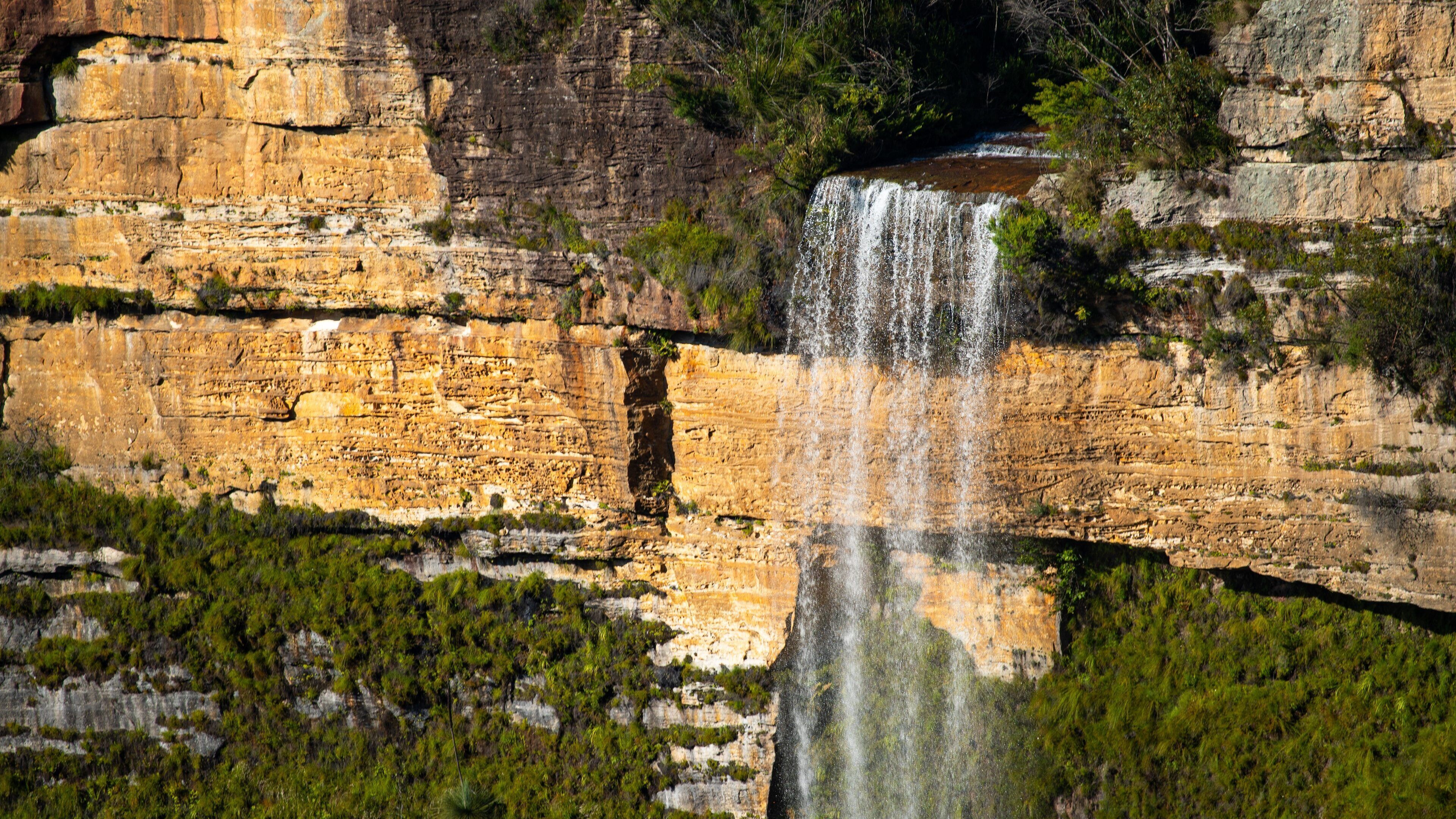 A waterfall cascading down a rocky cliff surrounded by greenery.
