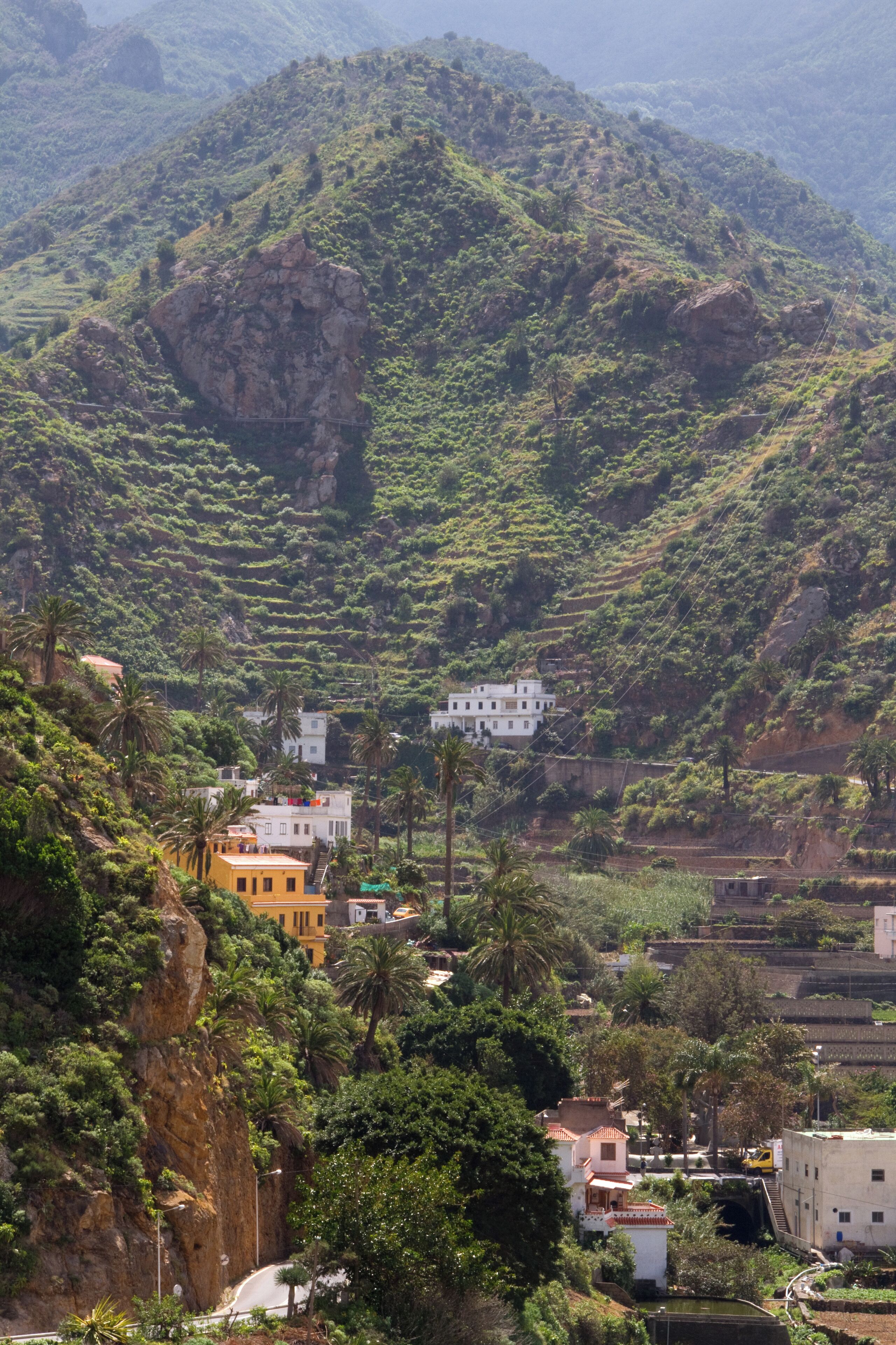 A mountainous landscape with terraced fields, a winding road, and scattered buildings.
