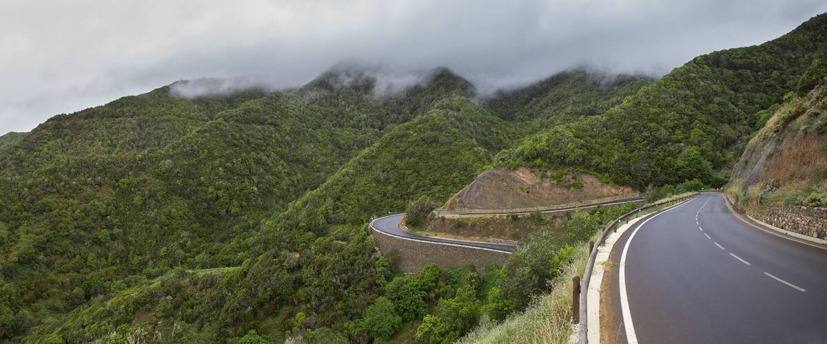 A winding mountain road surrounded by lush green hills and dense forest.