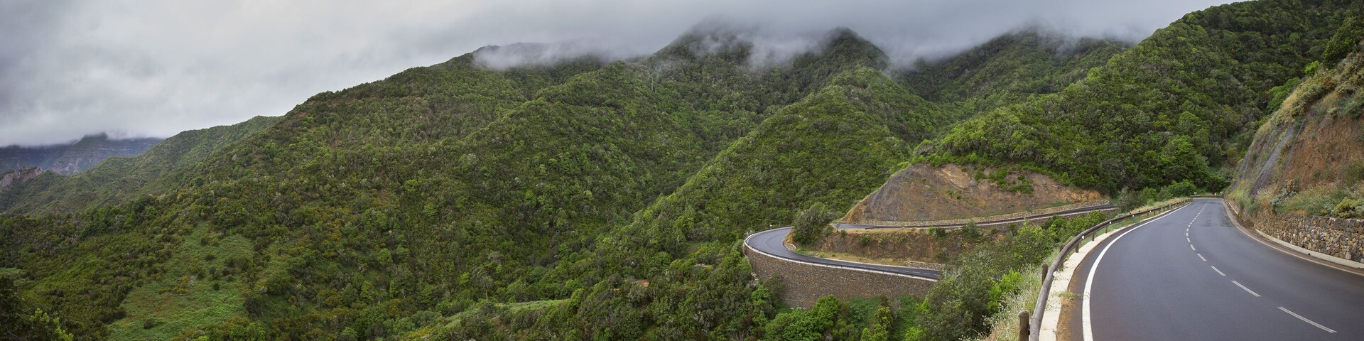 A winding mountain road surrounded by lush green hills and dense forest.