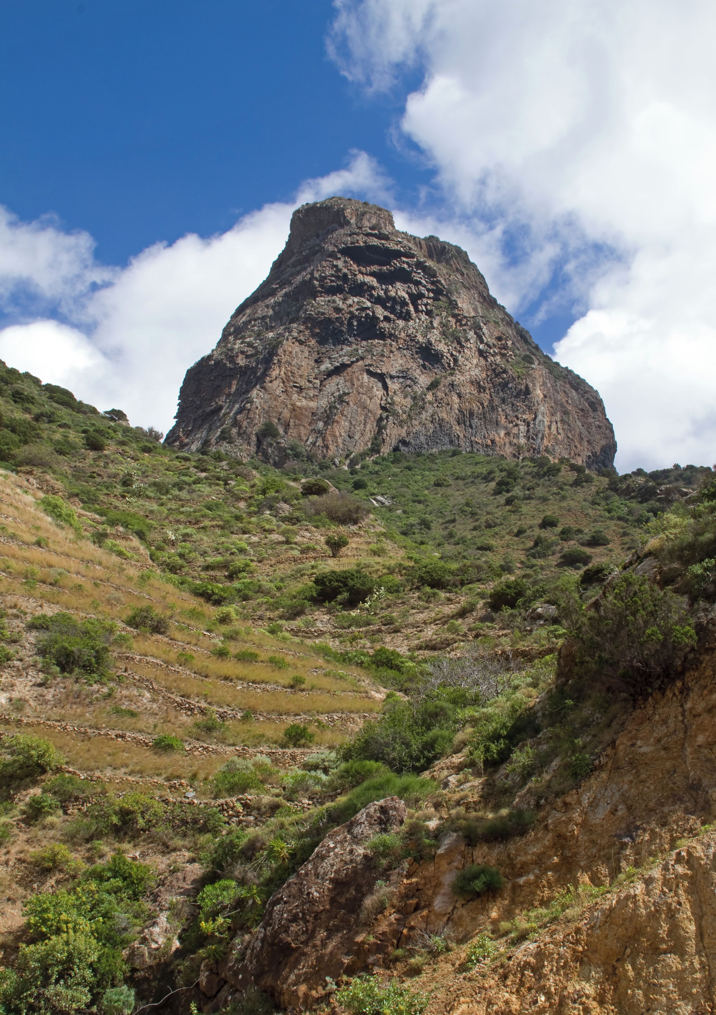 A rugged mountain with a prominent peak, surrounded by green vegetation and rocky terrain.