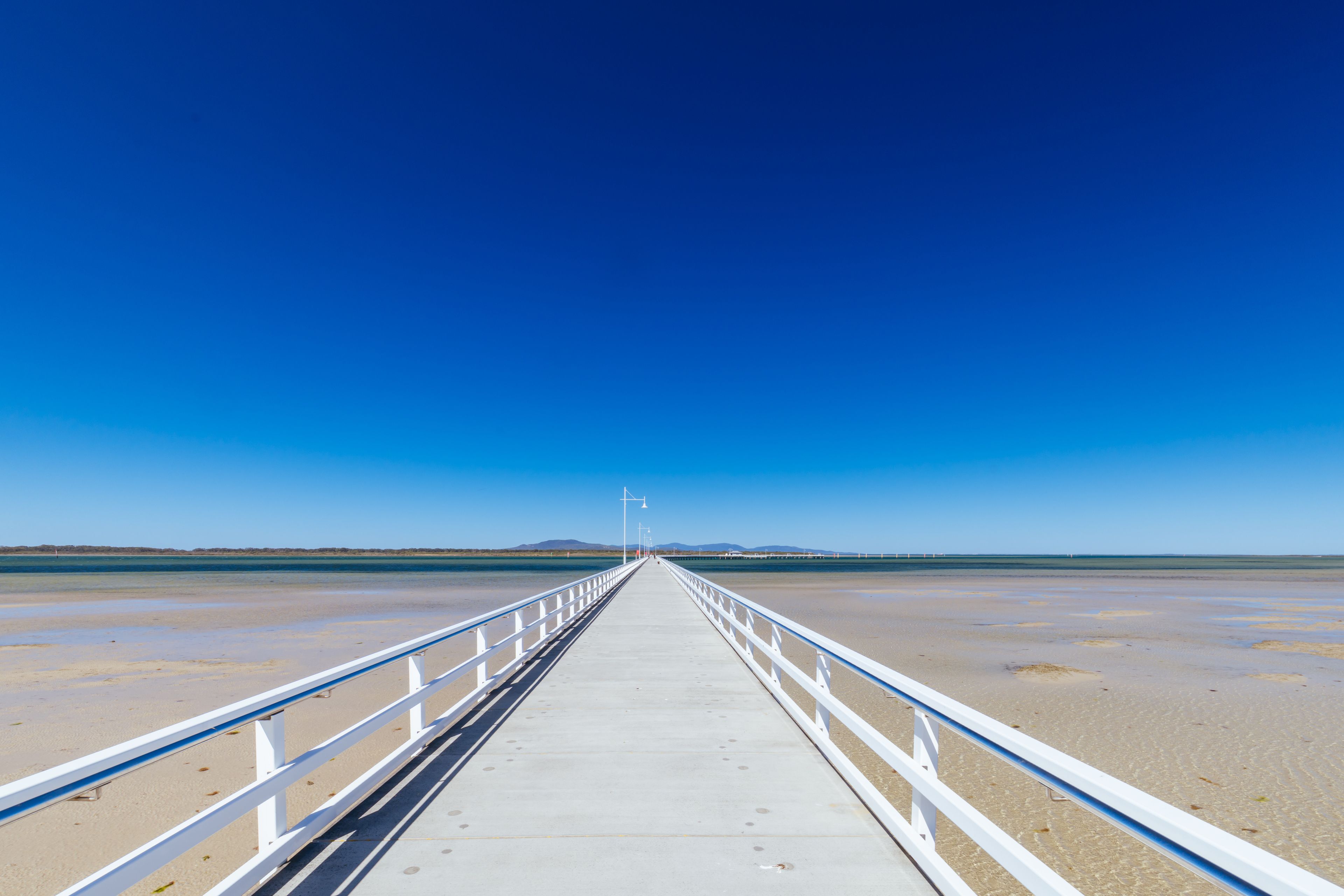 A long pier extending into a calm body of water with a clear blue sky above.