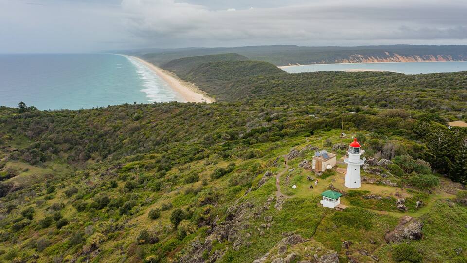 A coastal landscape with a lighthouse, beach, and hilly terrain.