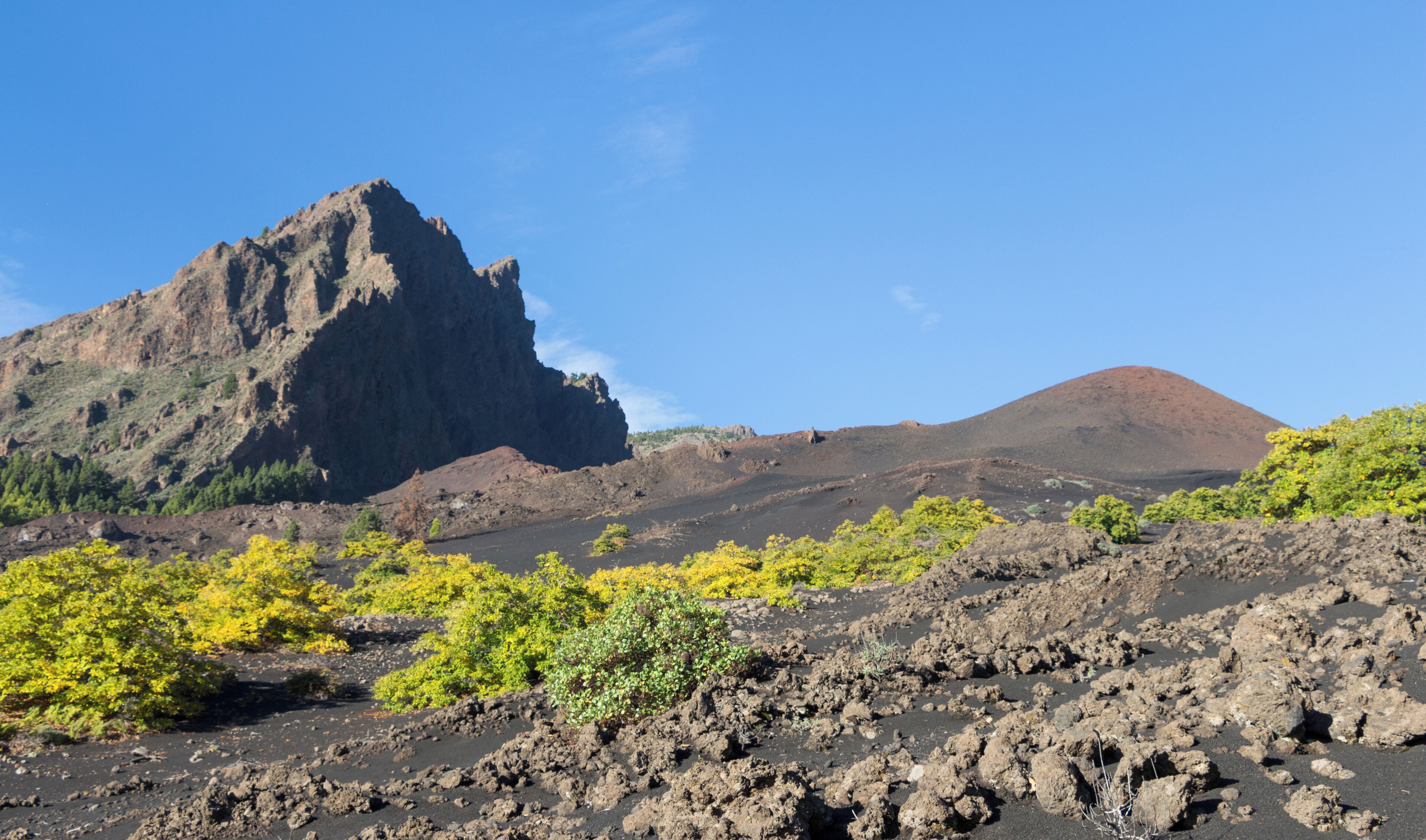 A volcanic landscape with rugged mountains, sparse vegetation, and a clear blue sky.