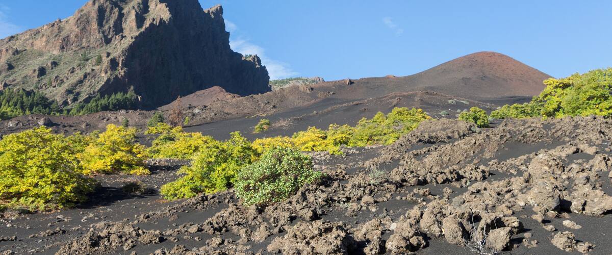 A volcanic landscape with rugged mountains, sparse vegetation, and a clear blue sky.