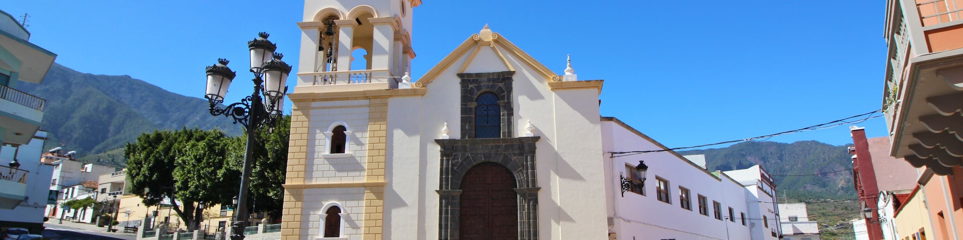 Una iglesia con un campanario, una calle con coches y una montaña al fondo.