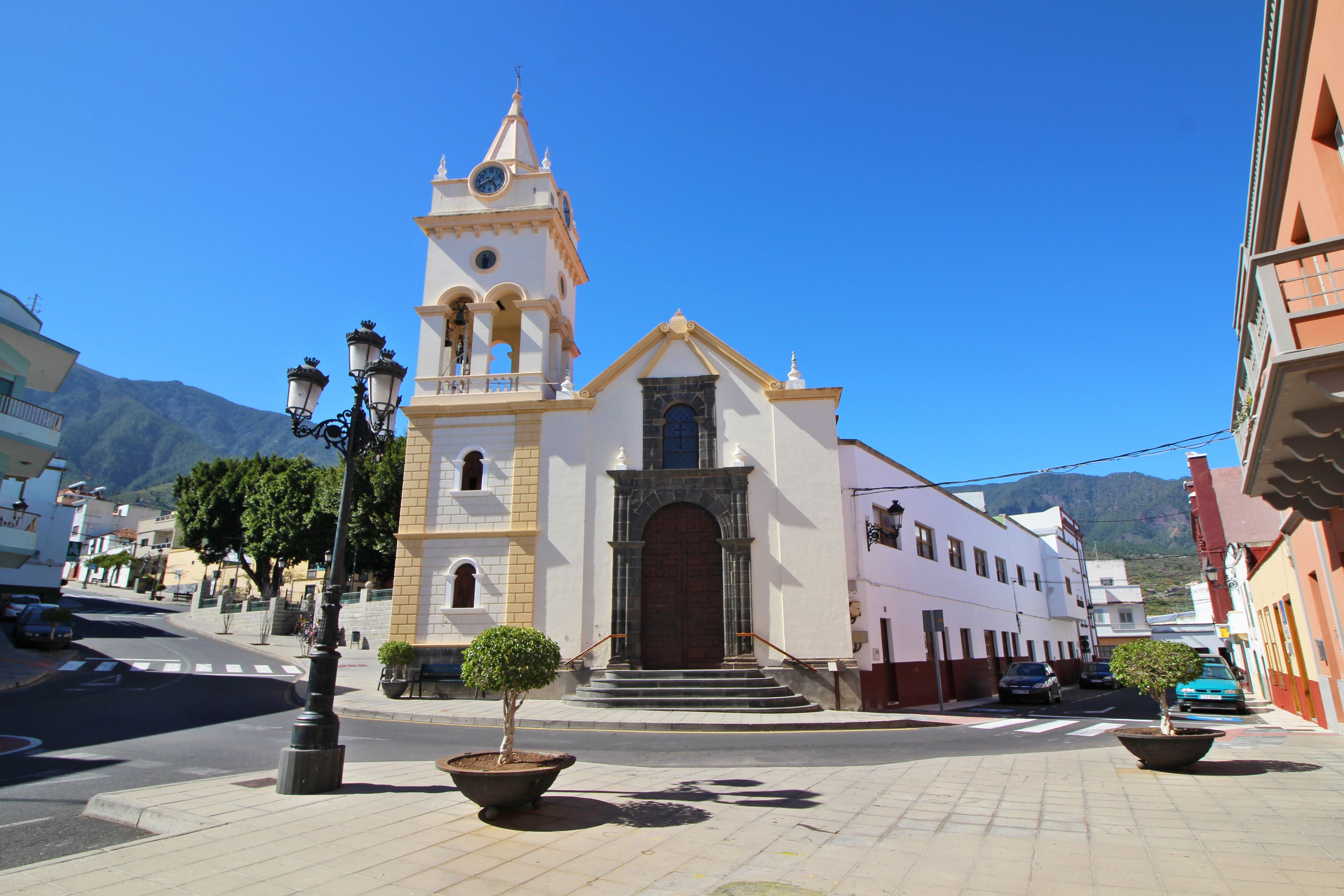 A church with a clock tower, a street with cars, and a mountain in the background.