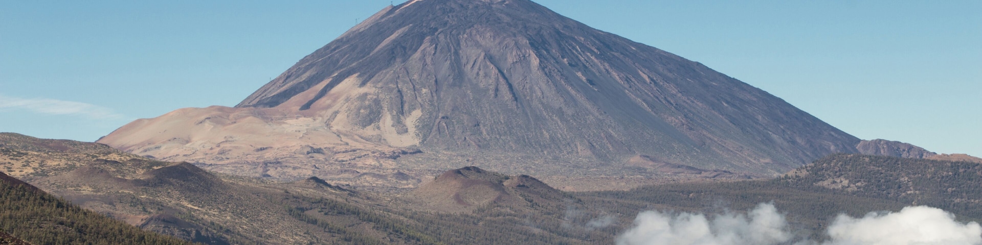 Una montaña de forma cónica, rodeada de colinas boscosas y un cielo despejado.
