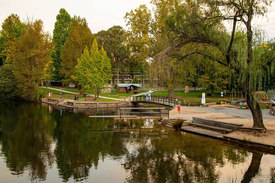 A park with a pond, a wooden bridge, and a stone building.