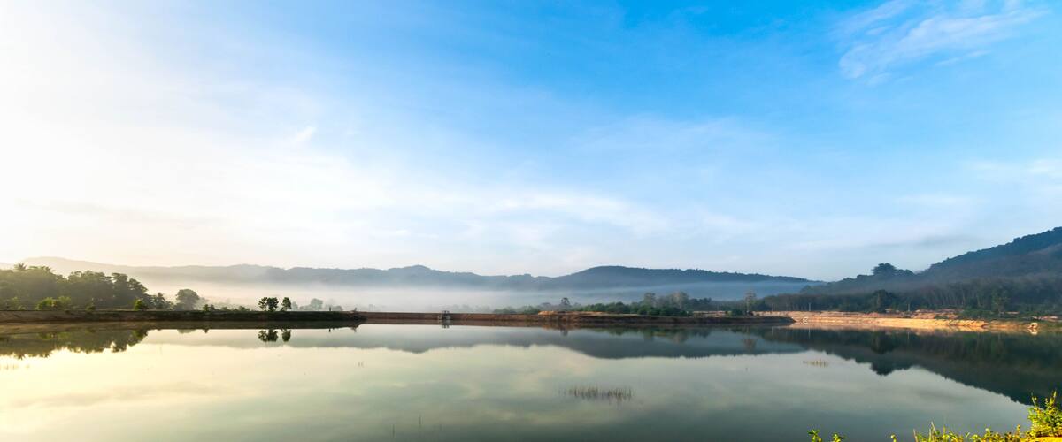 A calm lake with a misty mountain backdrop and a clear sky.