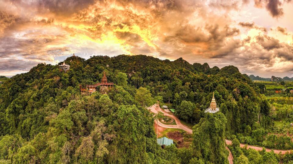 A lush green hill with a temple and a few buildings.