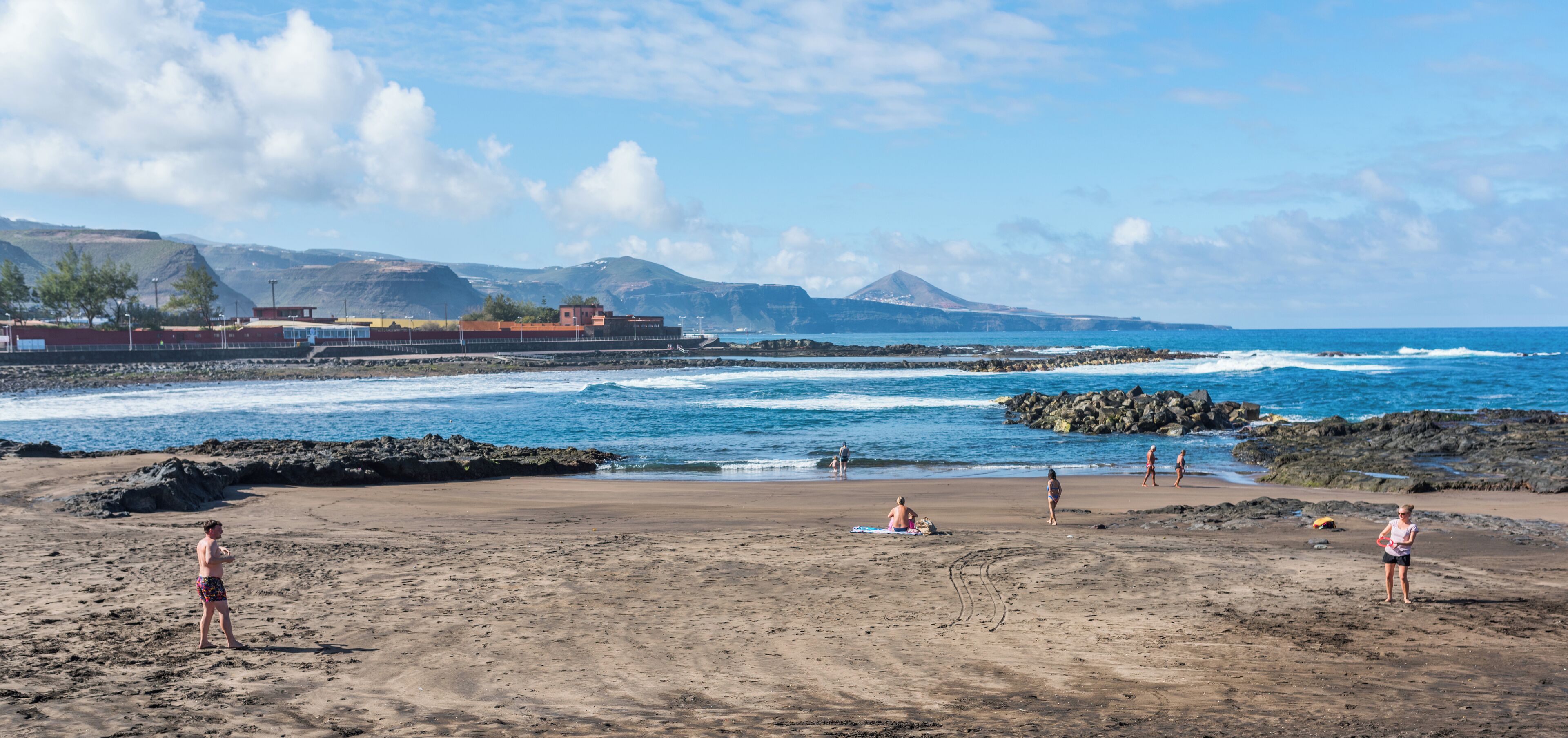 A beach with rocky shores, a clear sky, and distant mountains.