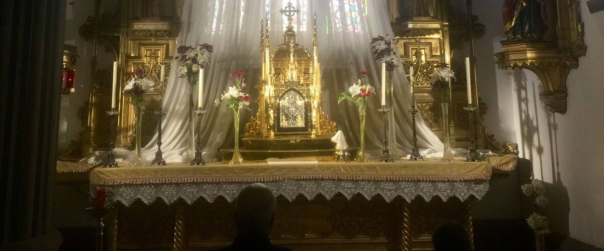 A church interior with a central altar, stained glass windows, and religious statues.