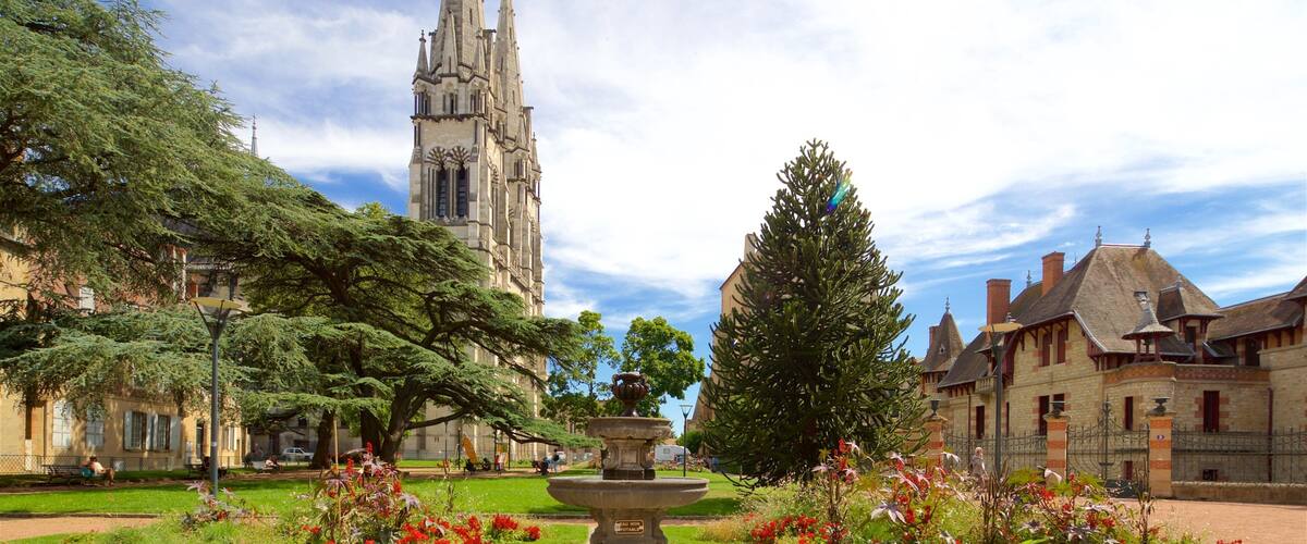A historic church with a tall spire, a central fountain, and surrounding lush gardens.