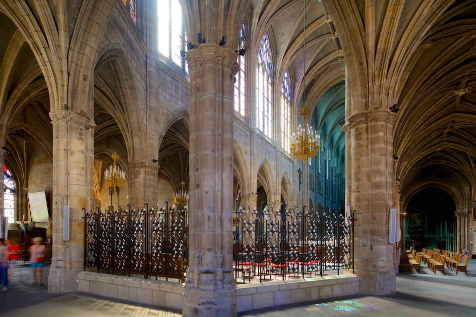 A cathedral interior with high vaulted ceilings, large stained glass windows, and a central aisle with rows of chairs.