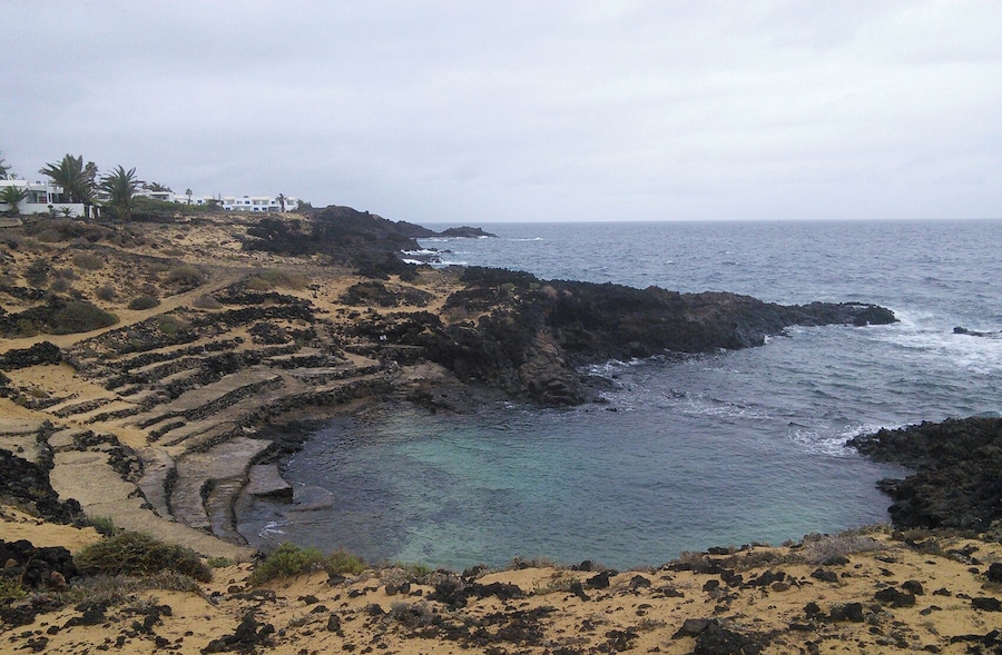 A coastal landscape with terraced fields, rocky outcrops, and a clear view of the ocean.