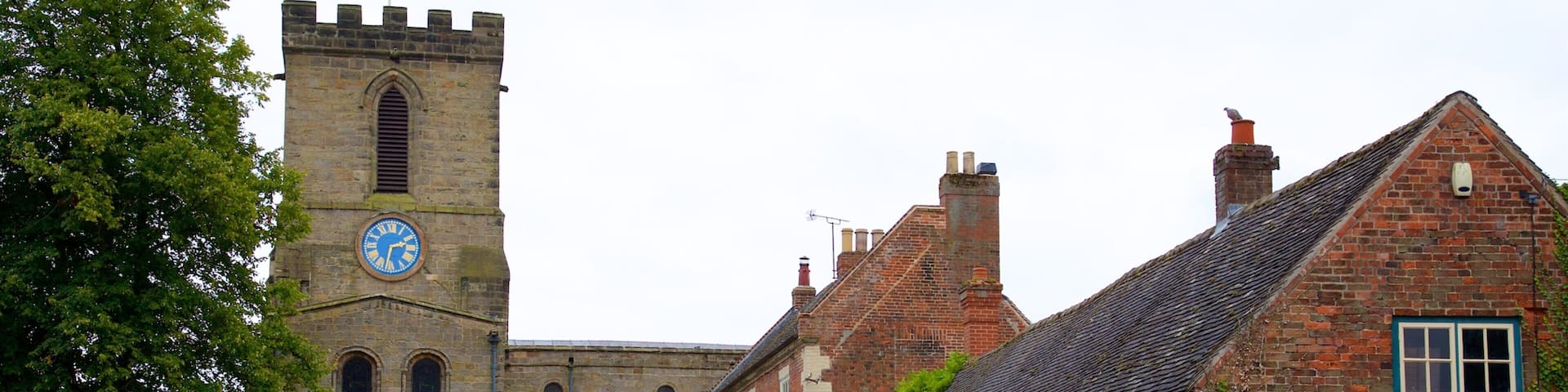 A historic church with a clock tower, a white van parked in front, and a sign for a butcher shop.