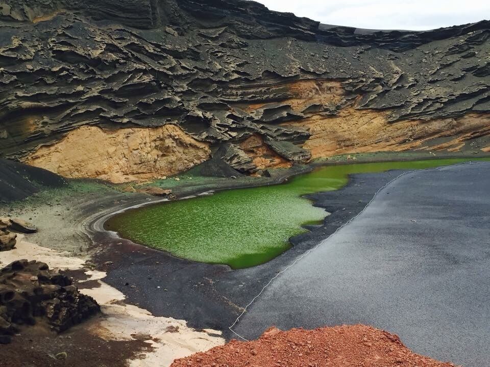 A short distance along the southwest coastline from the exciting Los Hervideros is a colourful natural example of the power of Mother Nature. El Golfo is a half-submerged cone of a volcano, which over time has been eroded by the sea, leaving behind only the striated wall of the crater displaying a myriad of red and russet colours.

At the foot of the crater wall is Lago Verde, a half-moon-shaped striking green lagoon filled with volcanic minerals and micro-organisms that are believed to be unique in this lake.

A beach of black volcanic pebbles, where you can look for specimens of the semi-precious olivine, superficially separates the sharply contrasting lagoon from the blue waters of the Atlantic Ocean, but in reality they are connected through underground passageways.

Coming from the south, the road leads you to a small car park, from where you can approach El Golfo by foot, following signs for a short walk around the headland.

A number of sheltered bays with black beaches link the lagoon with the tranquil El Golfo village, which attracts geologists and jewellery makers because of the olivine found in this area.

In addition, this small and peaceful community boasts several excellent seafood restaurants – great places to enjoy a tasty meal while enjoying a beautiful sunset and magnificent views.