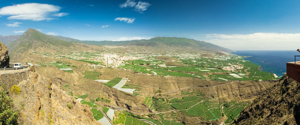 A mountainous landscape with terraced fields and a coastal view.