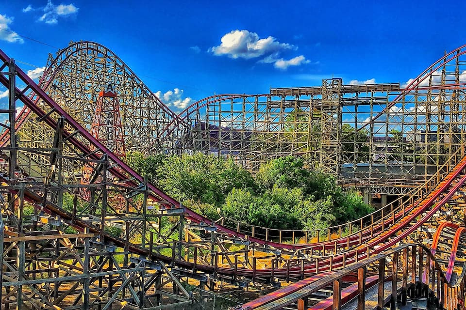 A roller coaster with a steep drop and multiple loops, surrounded by trees and a clear blue sky.