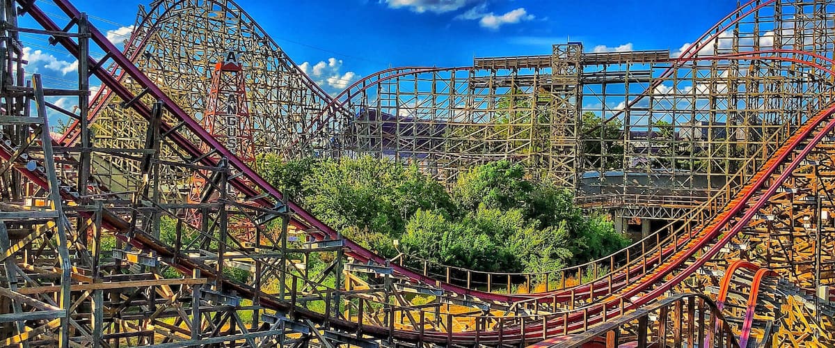 A roller coaster with a steep drop and multiple loops, surrounded by trees and a clear blue sky.