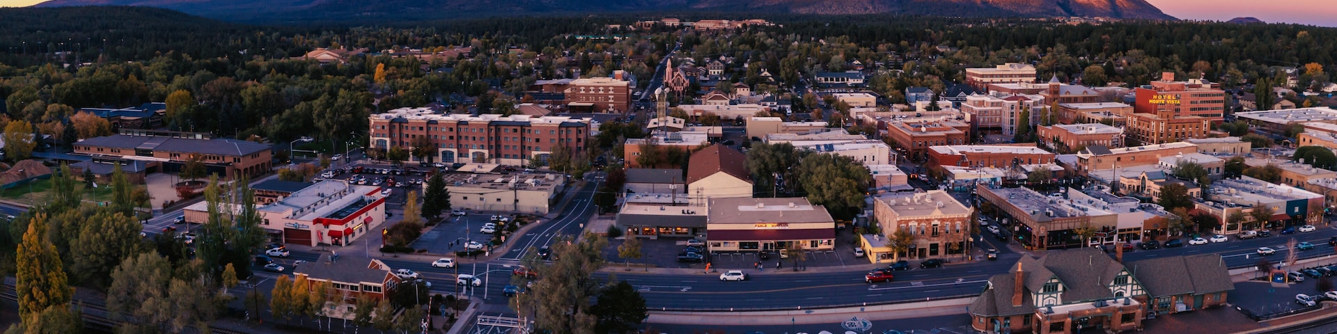 A town with a mountain backdrop, a railway crossing, and various buildings.