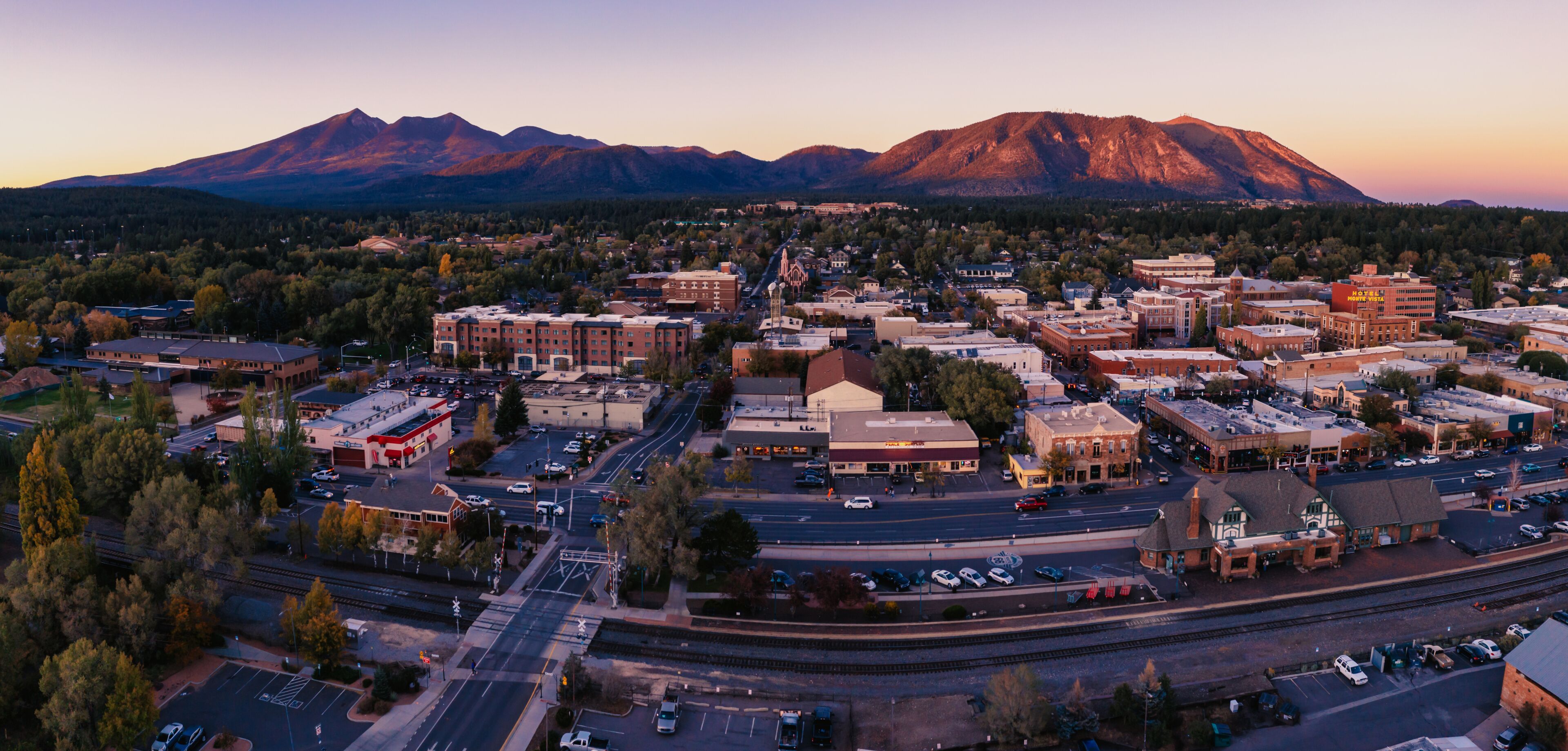 A town with a mountain backdrop, a railway crossing, and various buildings.