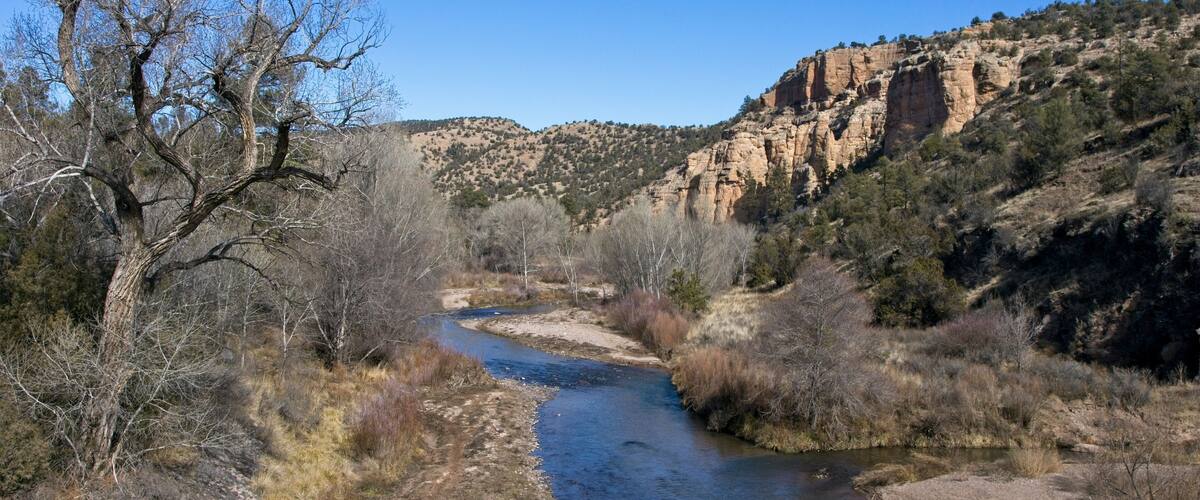 A river winding through a dry, rocky landscape with sparse vegetation and a prominent cliff in the background.