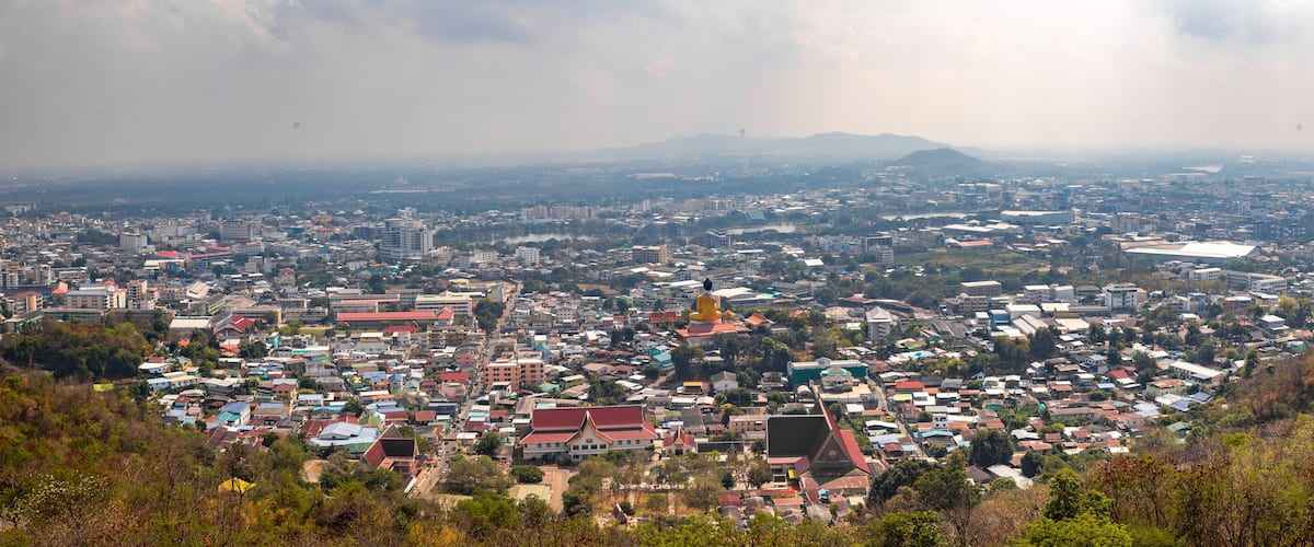 A cityscape with a prominent golden stupa, surrounded by residential and commercial buildings, under a cloudy sky.