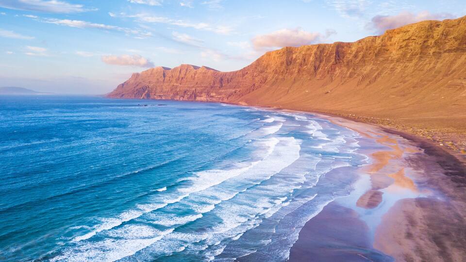 A coastal landscape with a sandy beach, ocean waves, and a cliff.