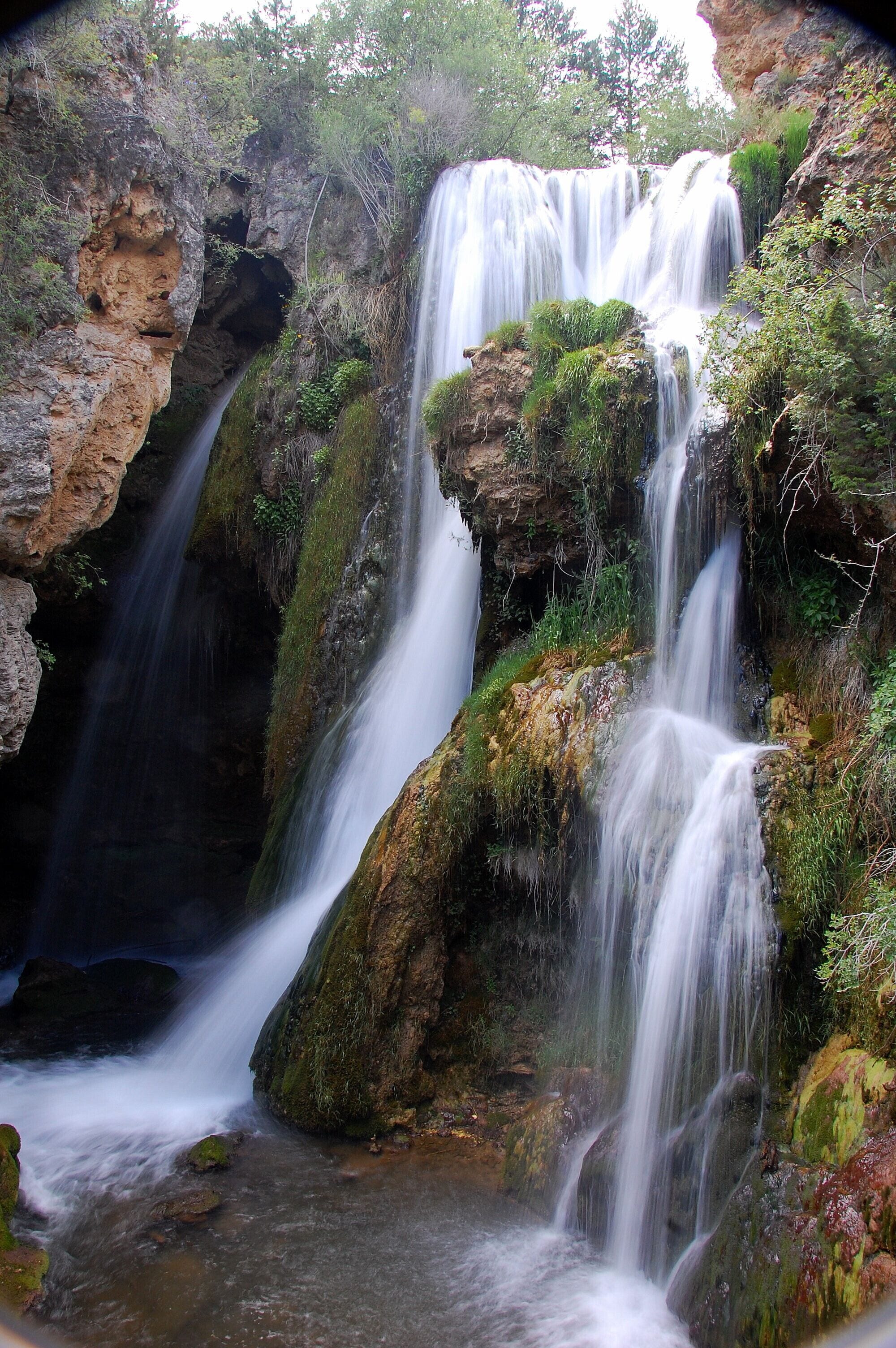 A multi-tiered waterfall surrounded by rocky terrain and greenery.