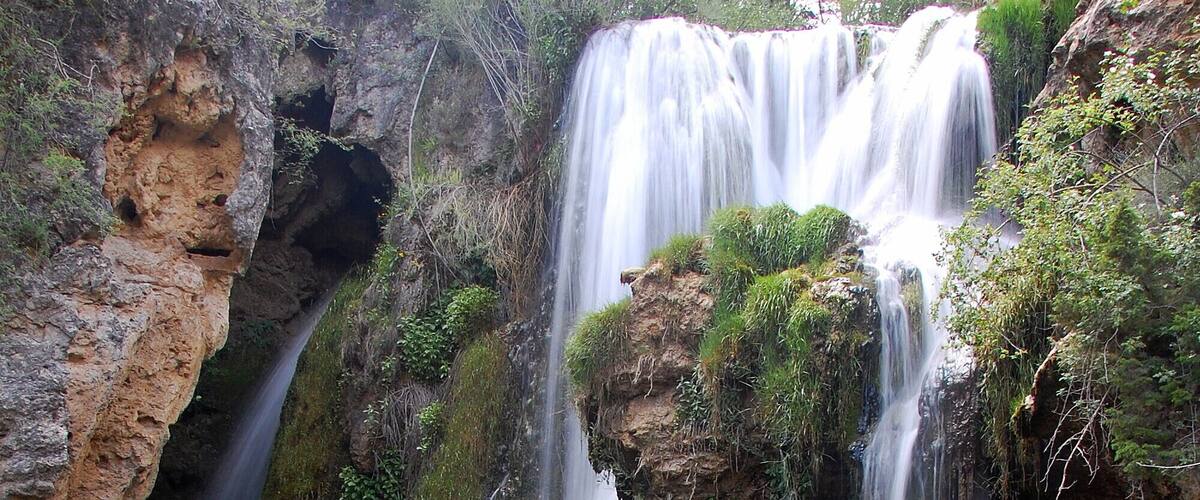 A multi-tiered waterfall surrounded by rocky terrain and greenery.