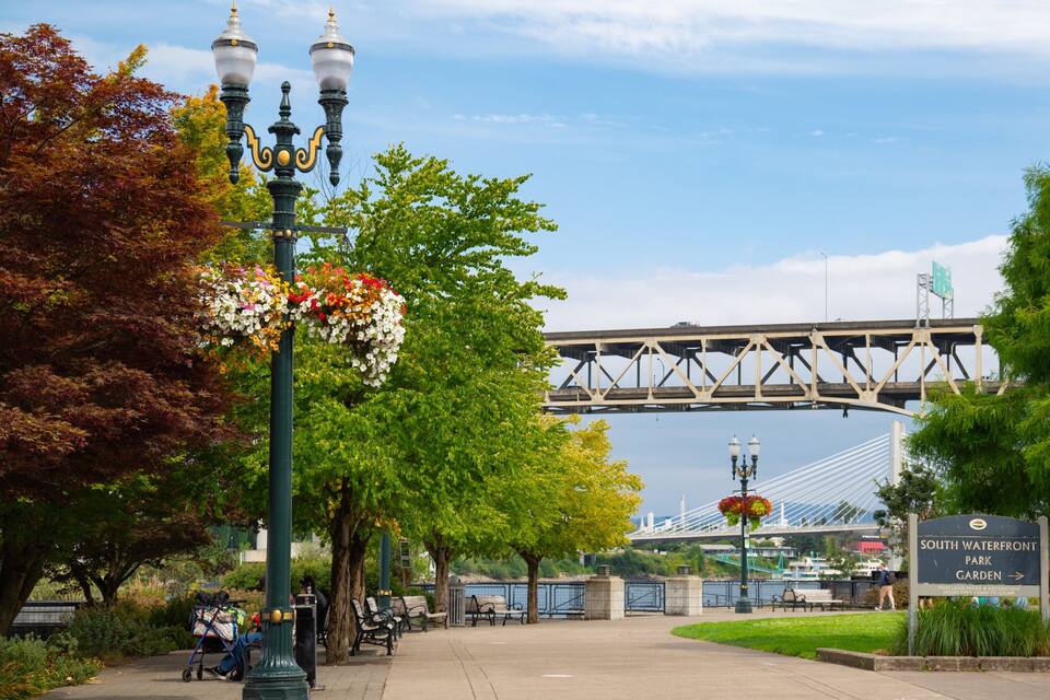Een park met bankjes, een brug en een bordje voor South Waterfront Park.