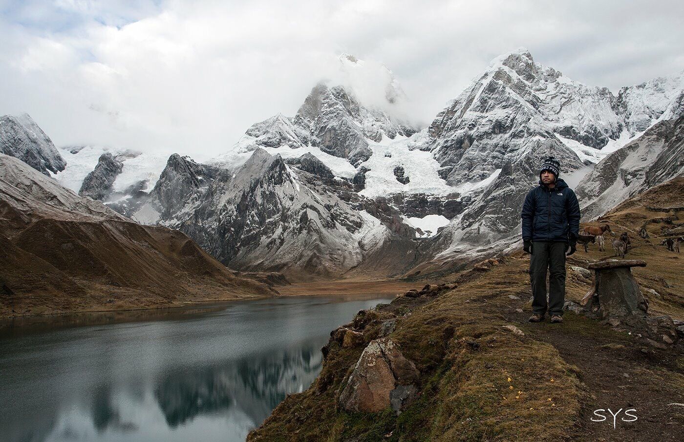 Una persona de pie junto a un lago rodeado de montañas nevadas.