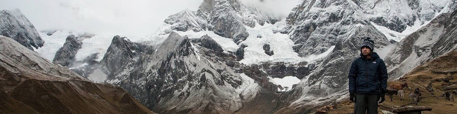 A person standing by a lake surrounded by snow-capped mountains.