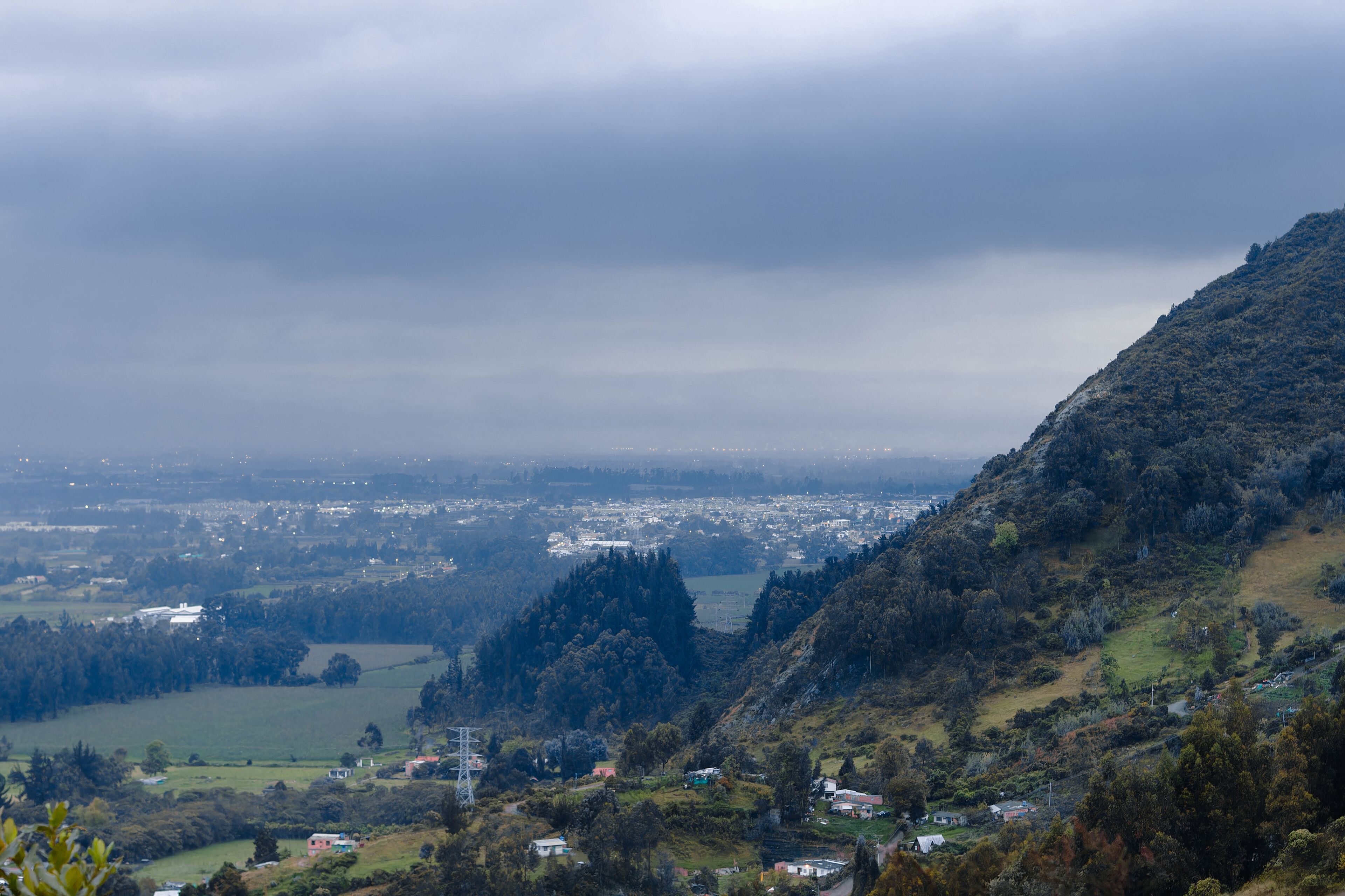 A mountainous landscape with a valley, scattered houses, and a distant city.