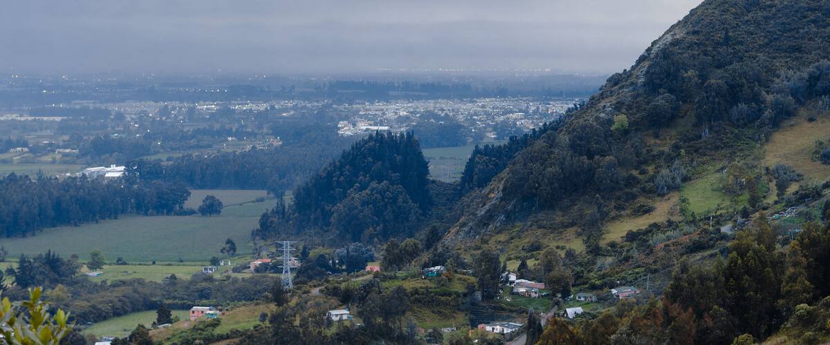 A mountainous landscape with a valley, scattered houses, and a distant city.