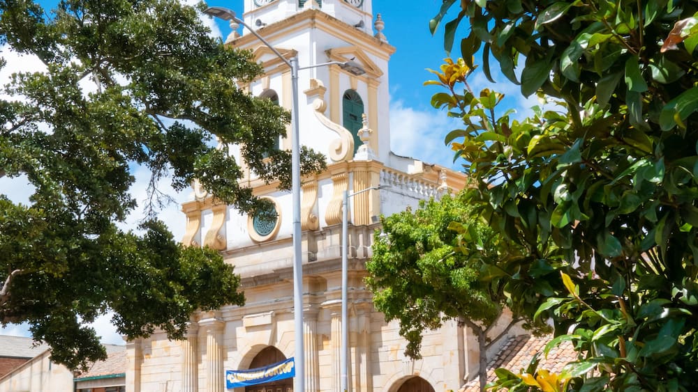 A historic church with a dome and clock tower, surrounded by greenery and a paved square.