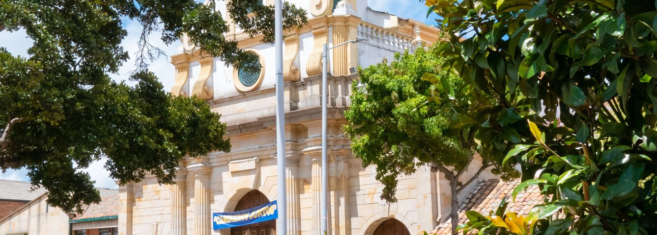 Una iglesia histórica con cúpula y torre del reloj, rodeada de vegetación y un adoquín.