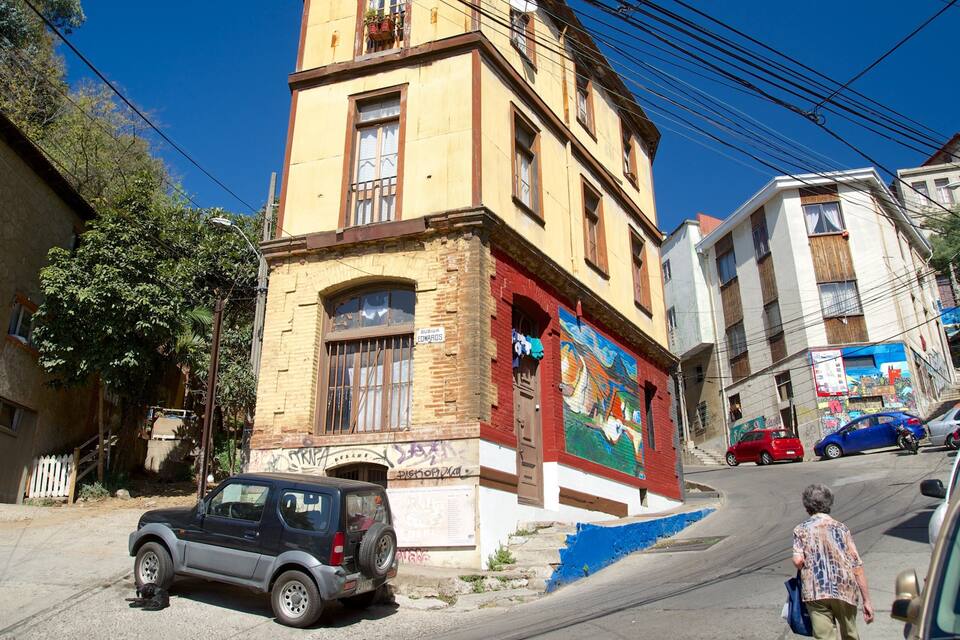 Una stretta via con un edificio giallo, un murale e auto parcheggiate.