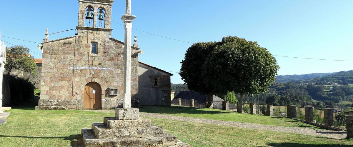 A historic church with a bell tower, a large cross, and a well-maintained lawn.