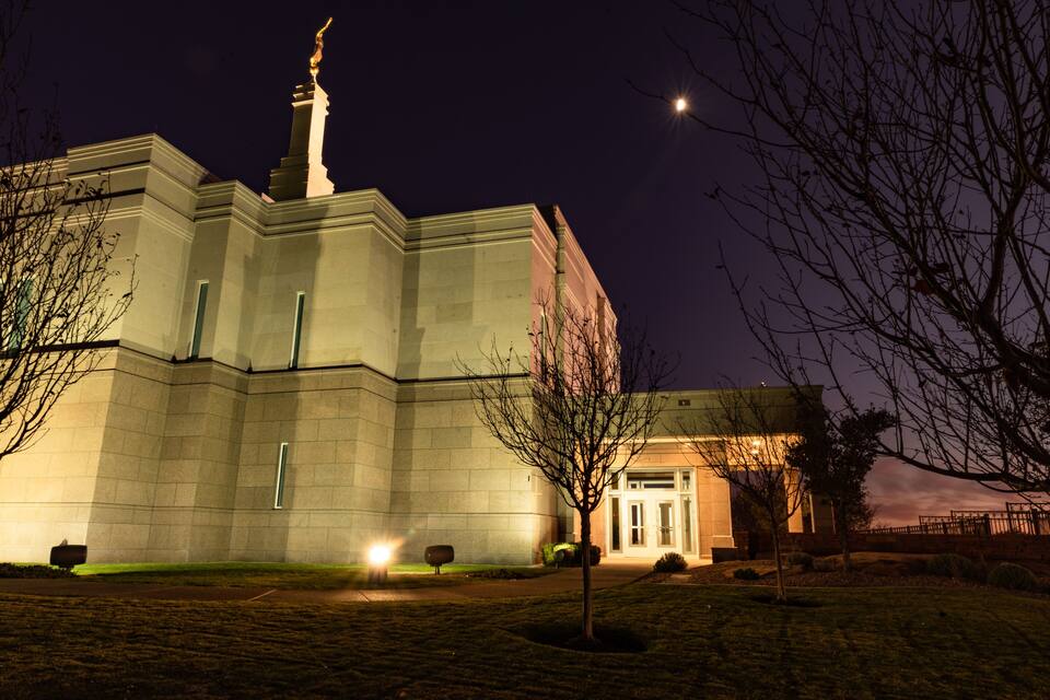 A large, illuminated building with a prominent tower and statue at night.