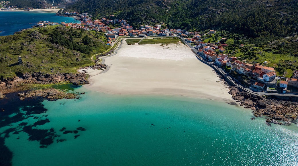A coastal town with a sandy beach, clear turquoise waters, and red-roofed buildings.