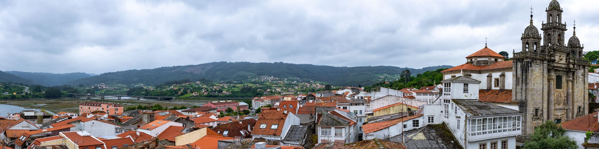 A historic town with terracotta-roofed buildings, a prominent church with a bell tower, and a river in the background.