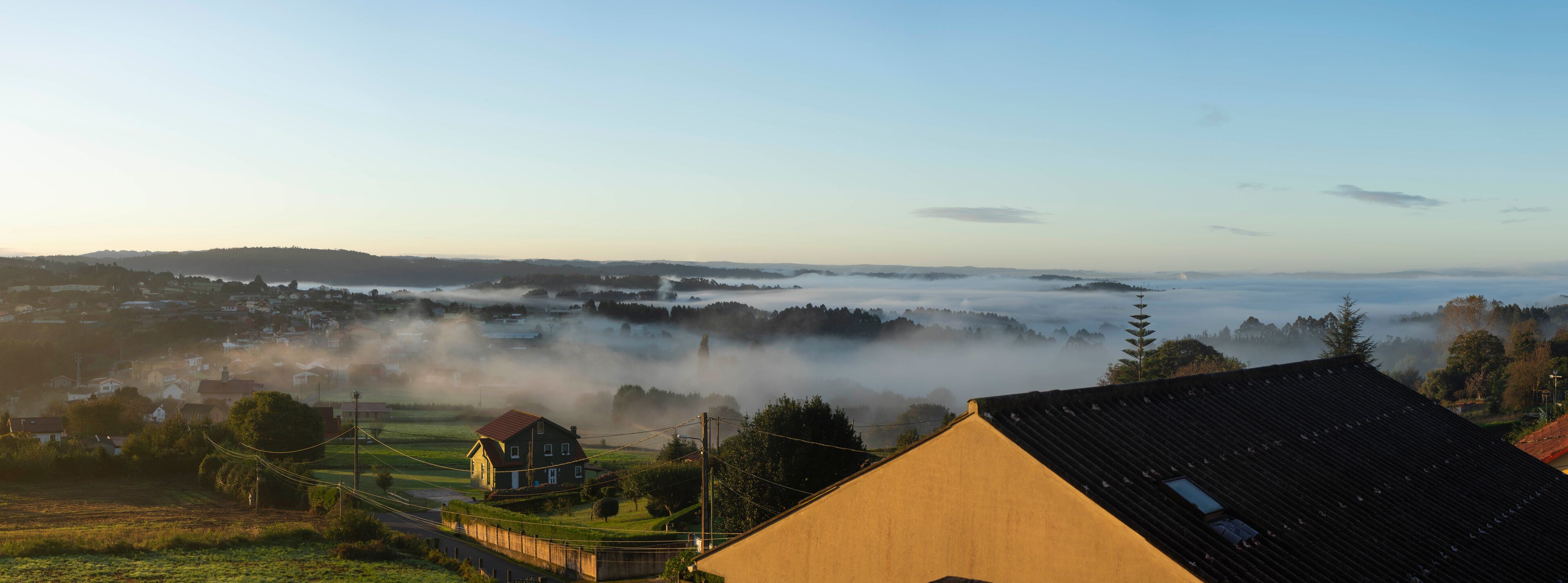 A foggy landscape with houses, a road, and a distant mountain range.