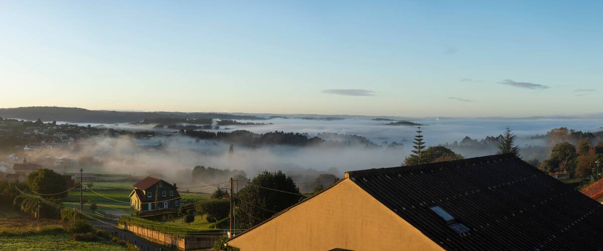 A foggy landscape with houses, a road, and a distant mountain range.